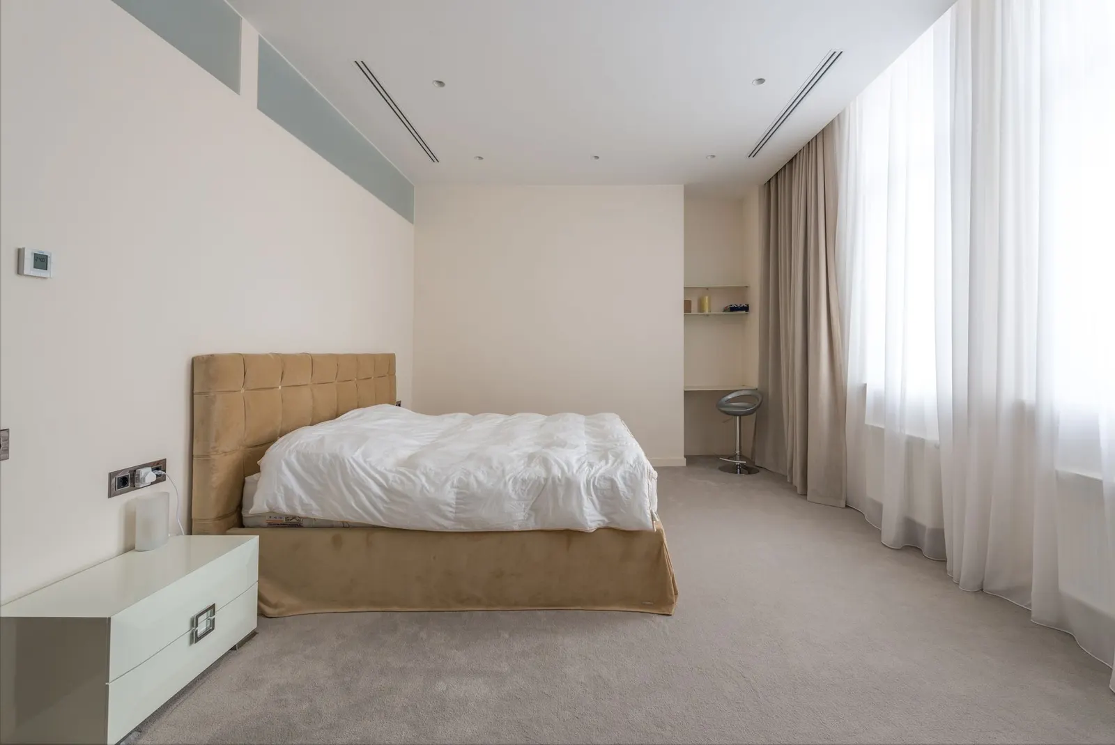 Large soft bed with white linen placed opposite window in light spacious bedroom in apartment in daytime