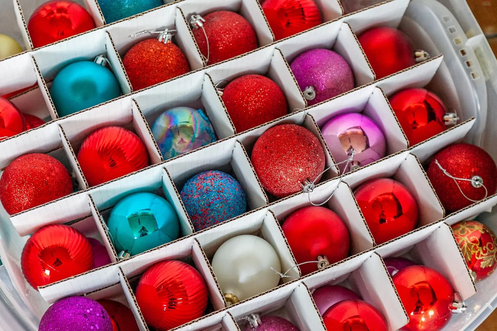 Clear storage bin holding Christmas ornaments in dividers and lights wound on cardboard