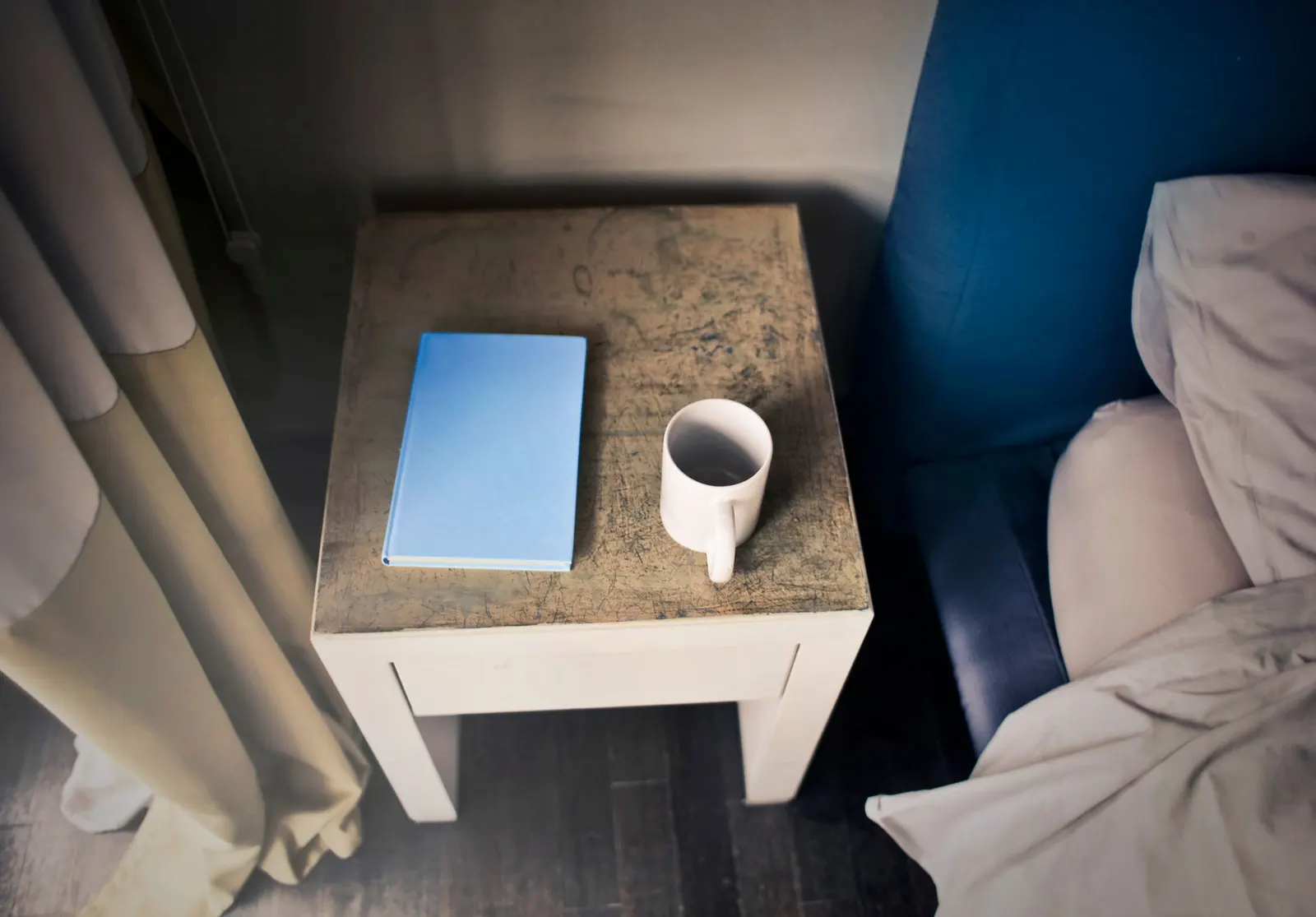 Small thrifted wooden side table painted a smoky blue next to a white armchair