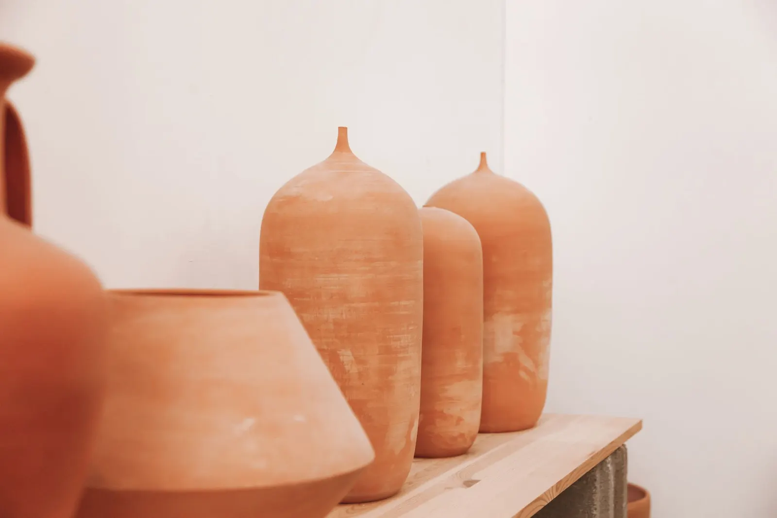 Shelf with terracotta and rosy-brown painted vases next to a cream wall