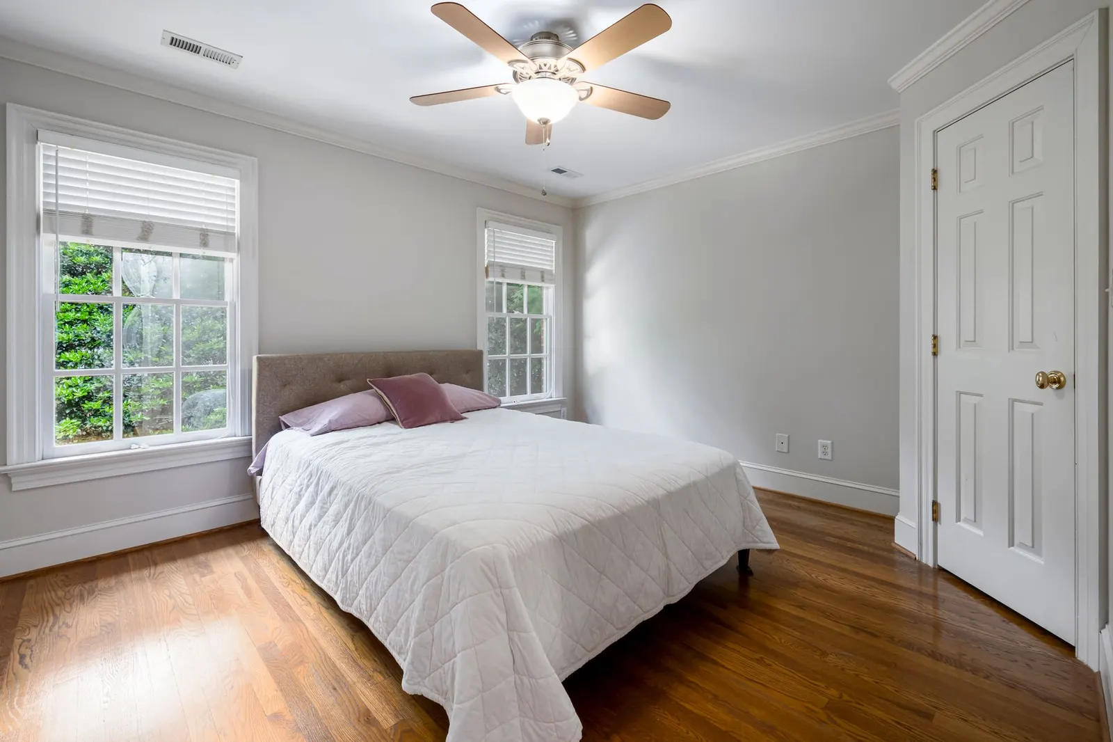 Tidy bedroom with white bedding, window blinds and a ceiling fan