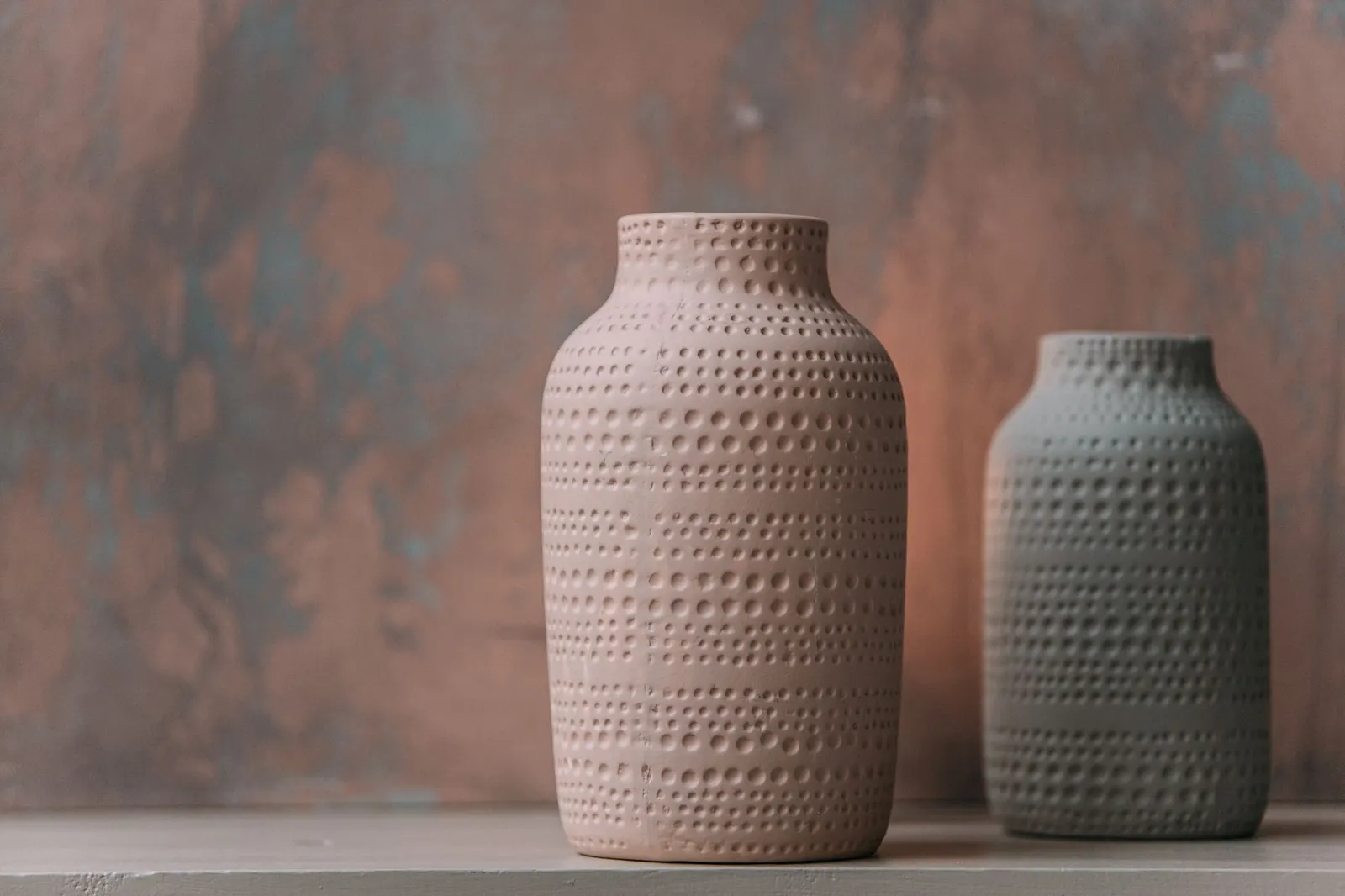 Three matte cream and greige textured vases with dried stems grouped on a wood shelf