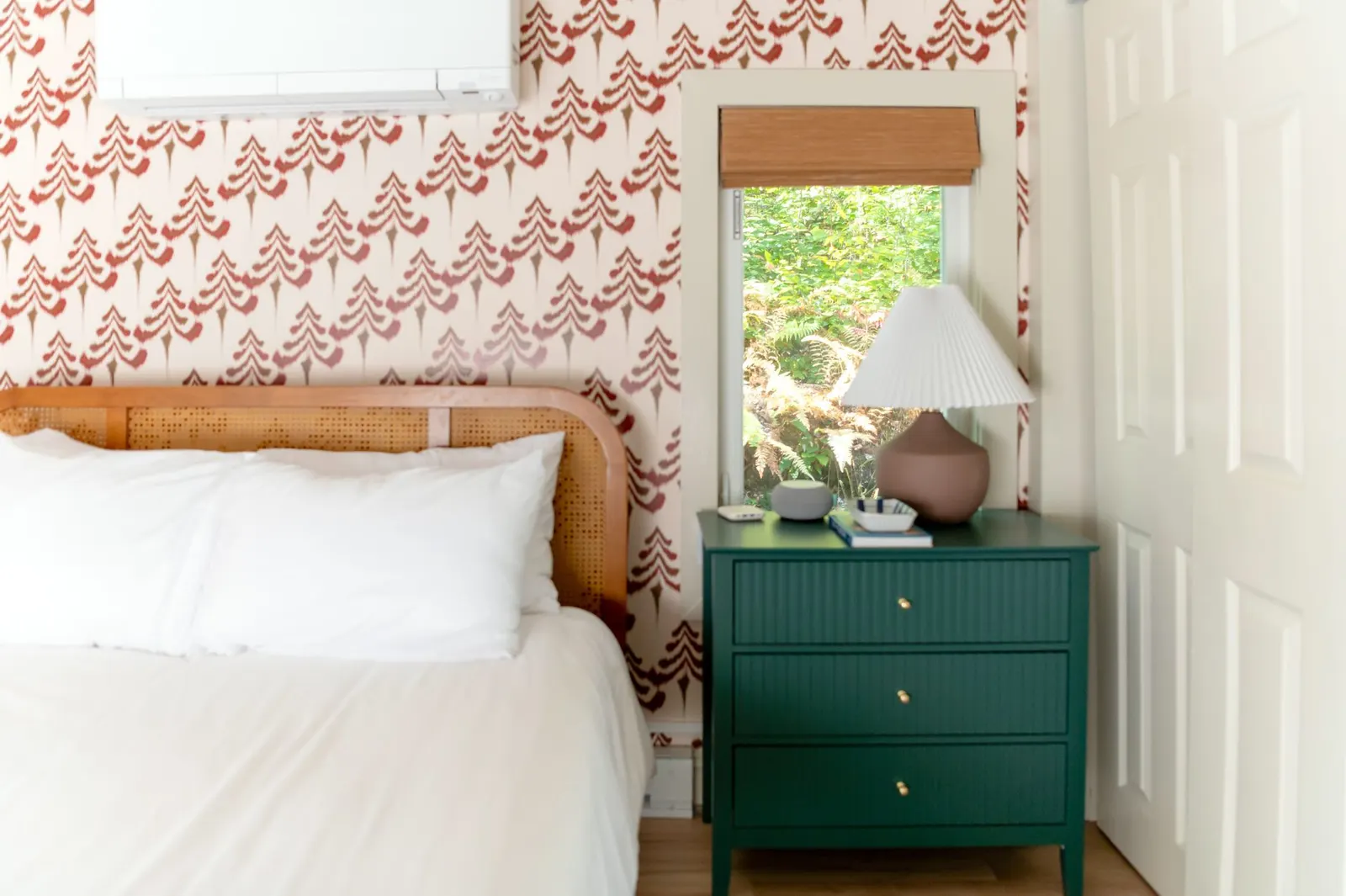 Sage green painted nightstand with brass knobs, a ceramic lamp and a stack of books beside a bed
