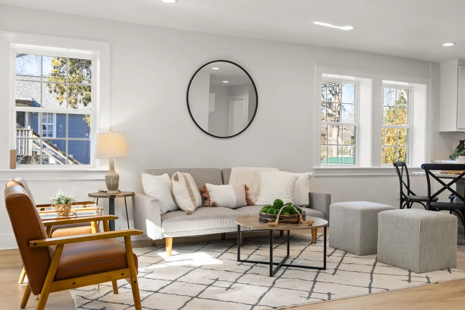 Round mirror with a thin wood frame on a side wall next to a bright window