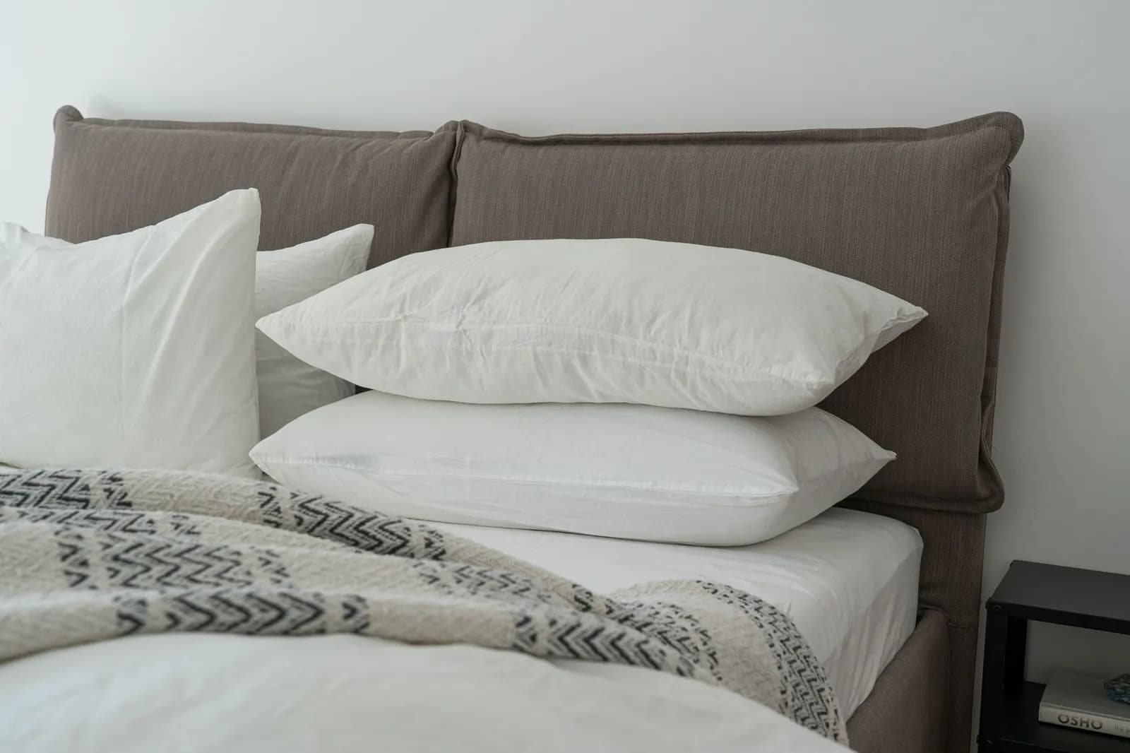 Guest bed made with white sheets, two stacked pillows and a gray knit throw folded at the foot