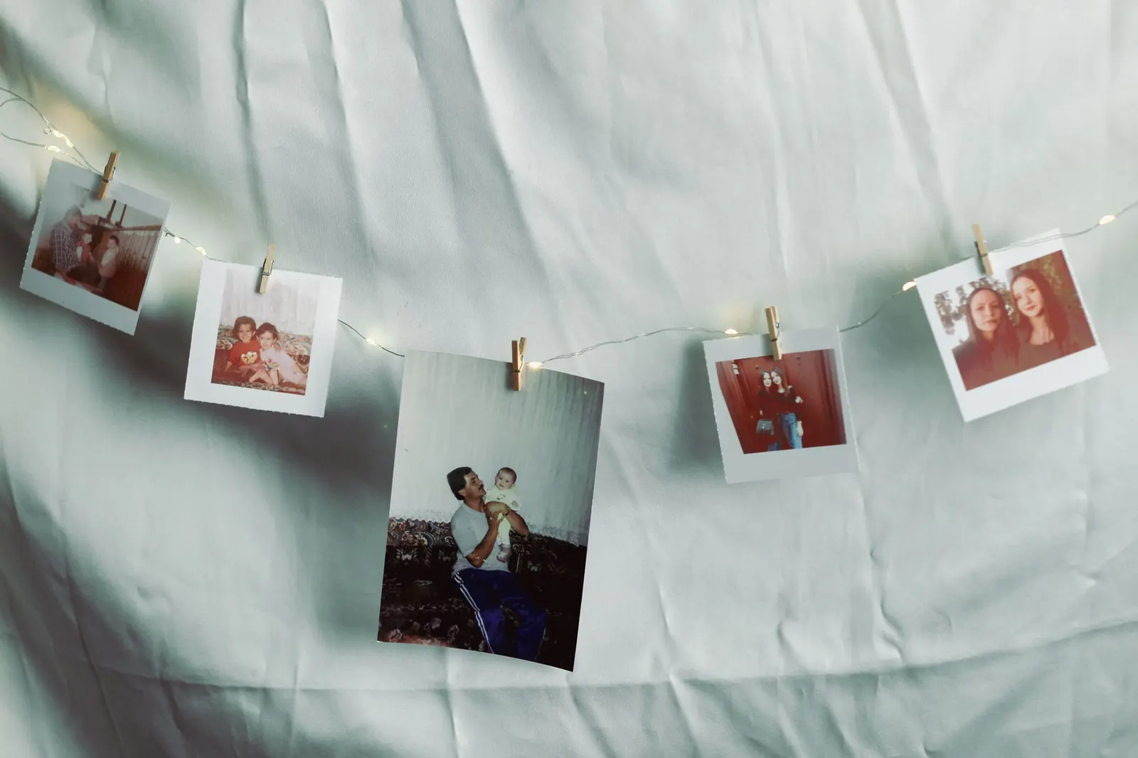 Unframed prints clipped to a strand of warm string lights on a white bedroom wall