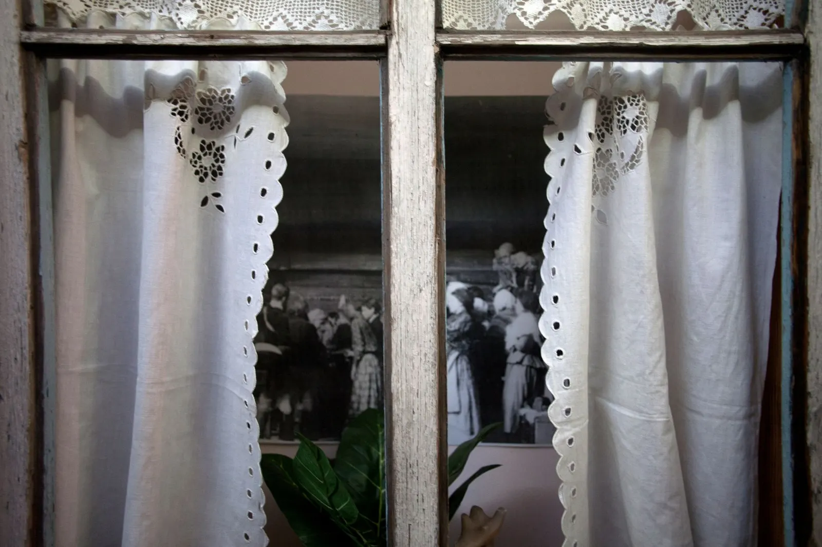 Short linen cafe curtain hung on a tension rod inside a white kitchen window frame