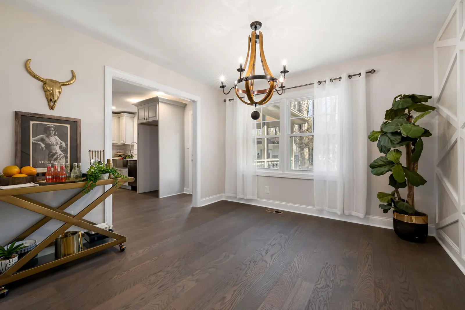 Bright living room with a gold bar cart, a tall plant and a chandelier