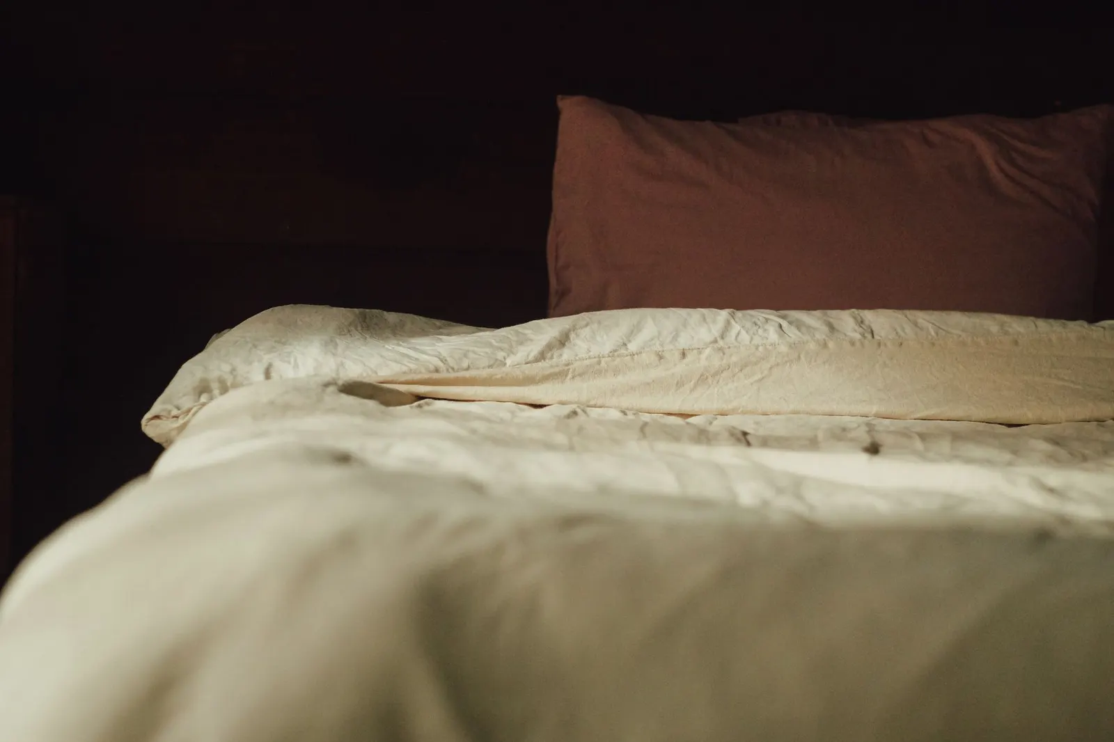 Bed with rumpled cream bedding and a brown pillow in soft light