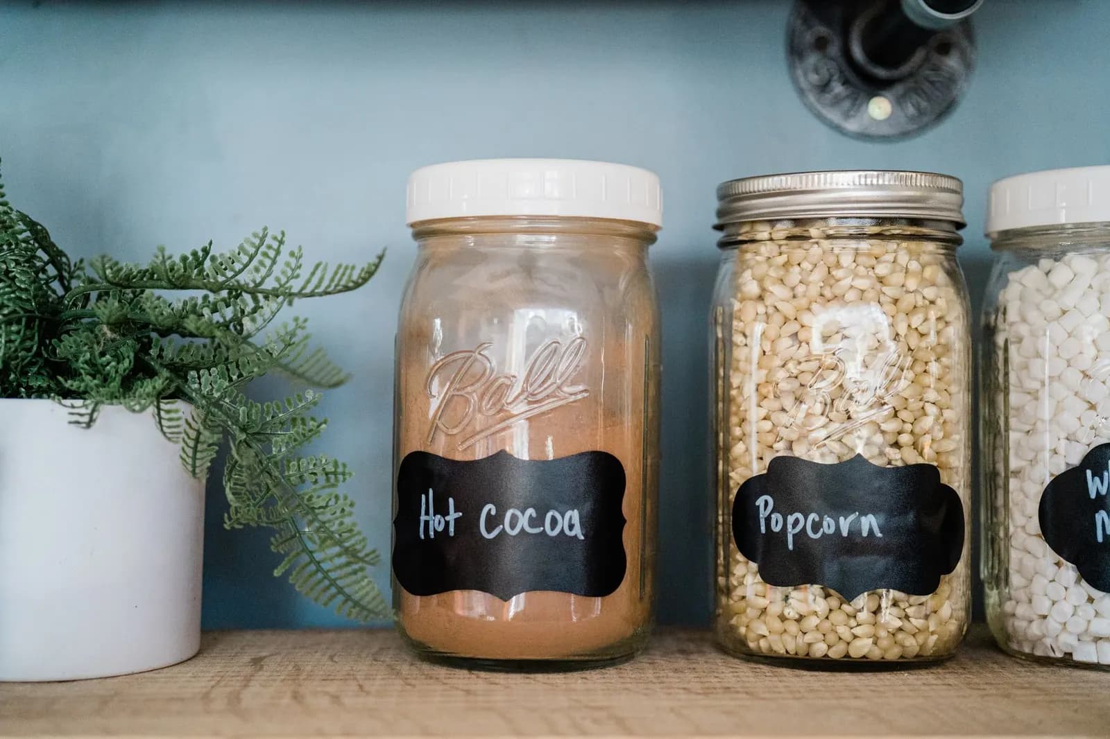 Glass jars of hot cocoa and popcorn with chalkboard labels on a pantry shelf