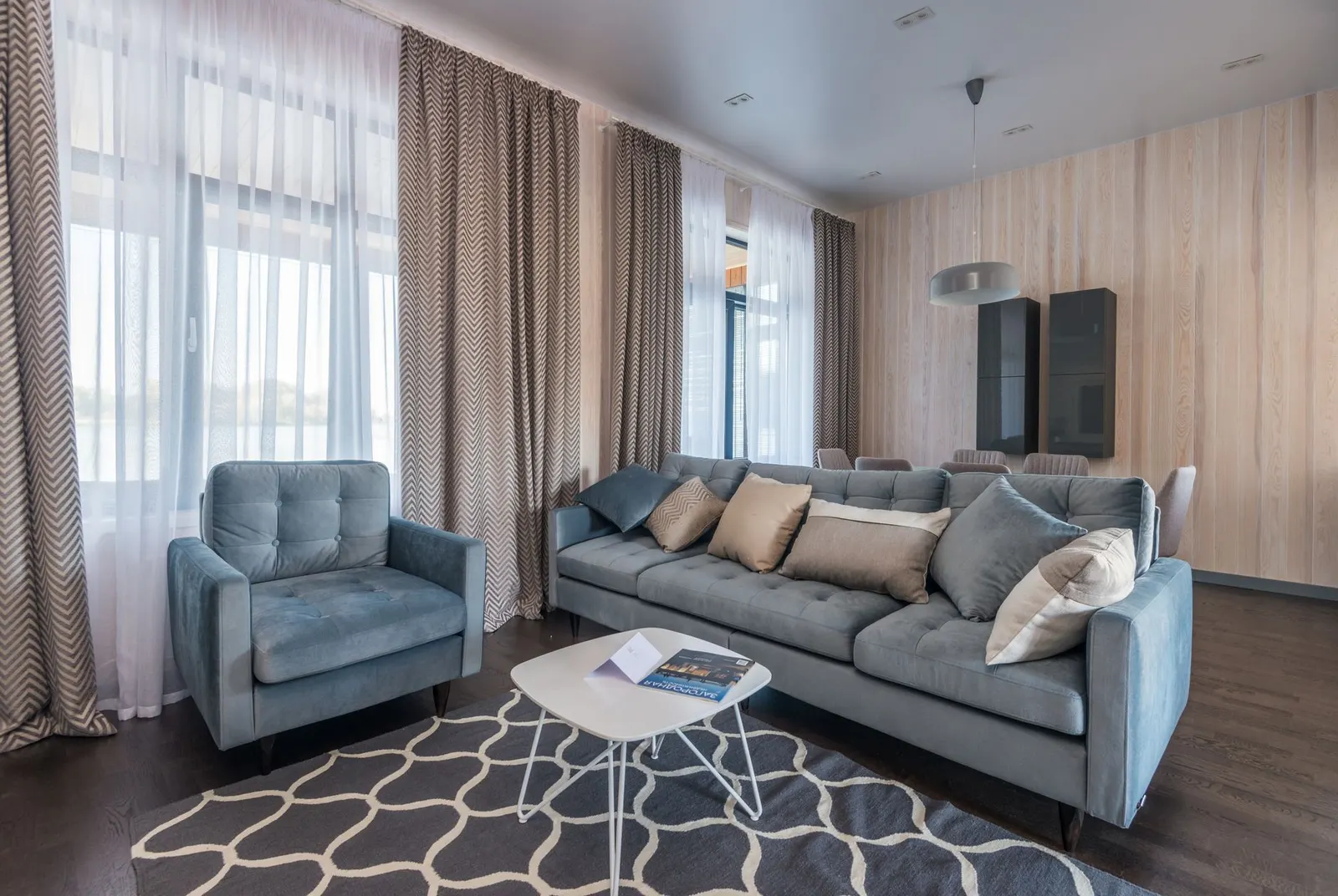 Elegant living room with blue sofa, armchair, and patterned curtains creating a cozy atmosphere.