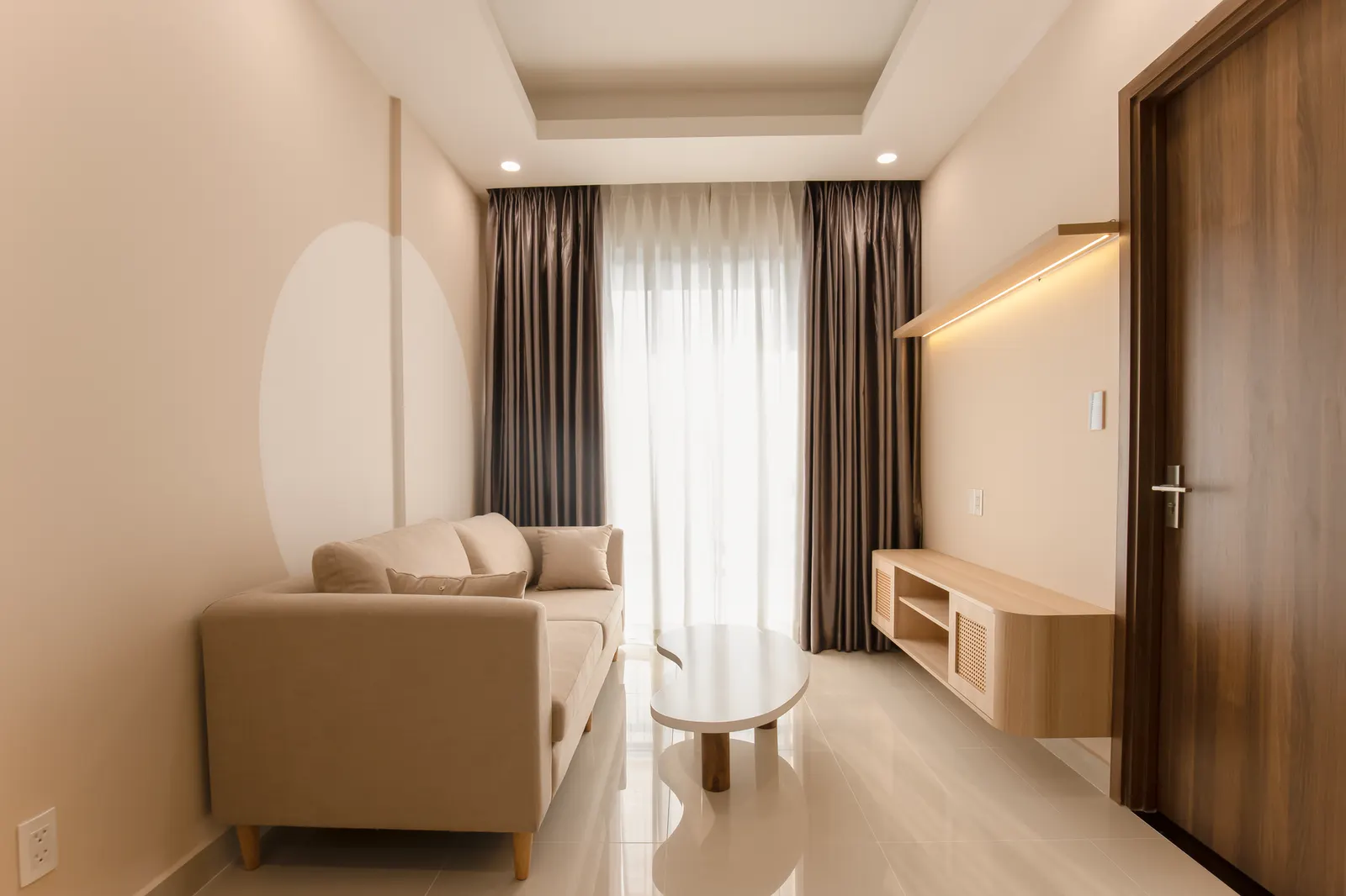A minimalist living room with a beige sofa, modern table, and soft lighting.