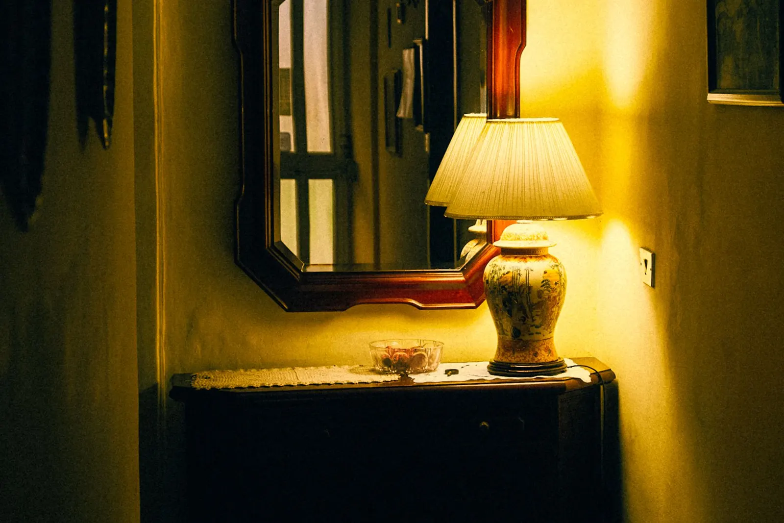 Warm, inviting corner of a room featuring an antique lamp, mirror, and table.